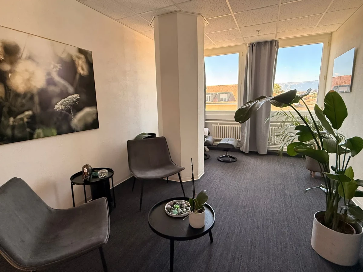 Vue d’ensemble du cabinet de Genève, avec fauteuils, plantes et grandes fenêtres donnant sur la ville.