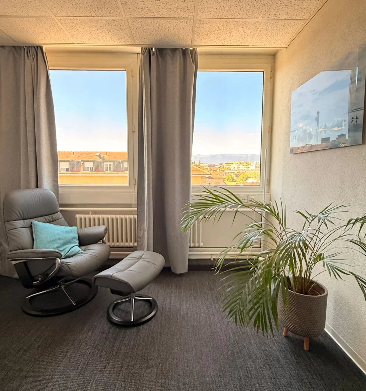 Fauteuil inclinable près des fenêtres du cabinet de Genève, avec plantes et vue sur les toits.
